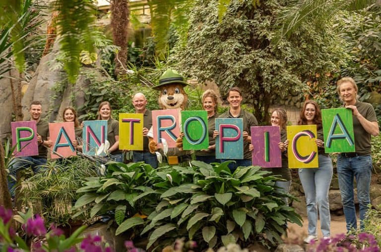 10 mensen naast elkaar die ieder een gekleurd bord met daarop een letter laten zien. Alle letters vormen de nieuwe naam Pantropica.