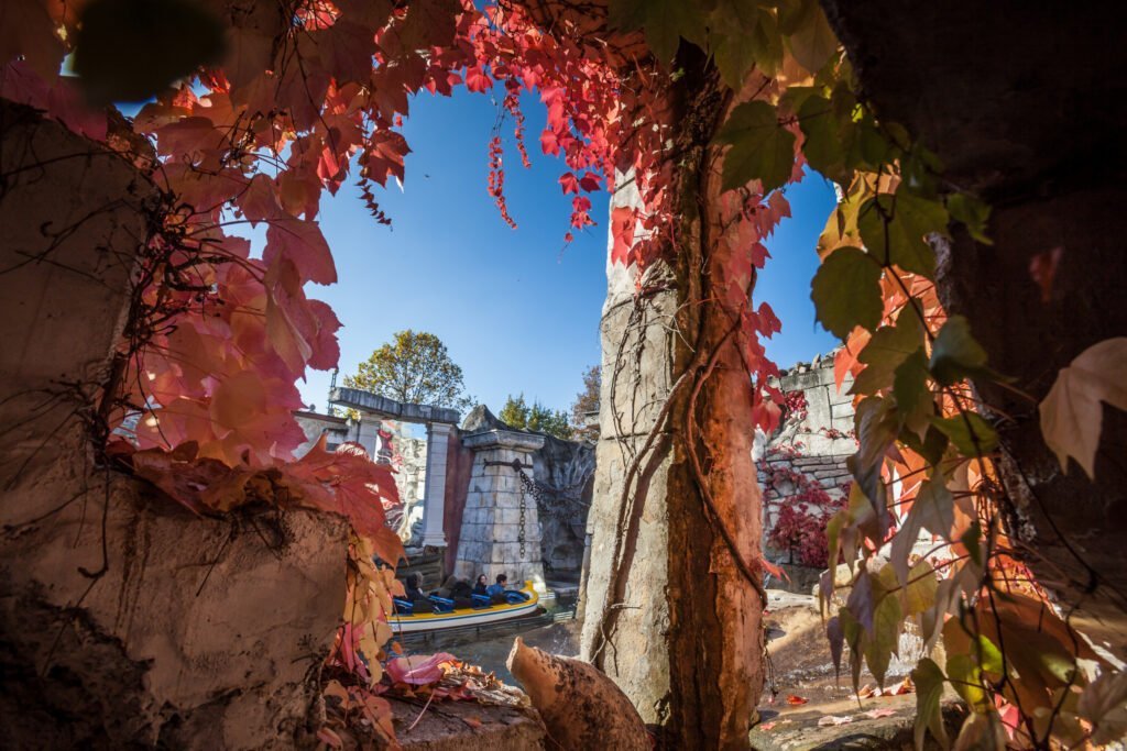 Een doorkijk met op de voorgrond herfstbladeren en een stenen pilaar. Op de achtergrond vaart het bootje van Poseidon met een blauwe lucht. Een frisse vaart tijdens Halloween.